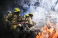 Firemen wearing yellow clothes extinguish fires that are extremely hot. There are both flames and smoke