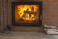 Fireplace with a blazing fire in the interior of a wooden house. Firewood and a fireplace set are located near the hearth with a Royalty Free Stock Photo