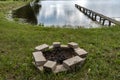 A fireplace made of bricks on the green bank of the pond and a wooden footbridge