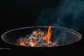 Firewood burns in a round barbecue at night. Dark background. Preparing to cook food on the grill Royalty Free Stock Photo