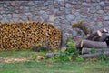 Firewood neatly stacked near a stone wall, green grass and chopped logs Royalty Free Stock Photo