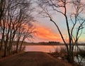 Firey orange sunset clouds at dusk over lake fishing access boat launch with bare winter trees Royalty Free Stock Photo