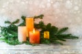 First Advent, arrangement with four candles in orange and yellow, one is lit with a flame, fir branches on light rustic wood,