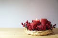 First advent with four red candles, one of them lighted, in a natural willow wicker wreath with berry decoration, seasonal home