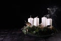 First Advent - Advent wreath from fir and evergreen branches with blown out candle on dark wooden table. White smoke on black