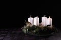 First Advent - Advent wreath from fir and evergreen branches with white burning candles on dark wooden table. Black background. Royalty Free Stock Photo