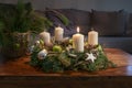 First Advent, wreath with one burning white candle and Christmas decoration on a wooden table in front of the couch, festive home