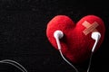 First aid band cushioned plaster strip medical patch glued on red heart with earphone listen to music on wooden background. Heart Royalty Free Stock Photo