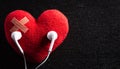 First aid band cushioned plaster strip medical patch glued on red heart with earphone listen to music on wooden background. Heart Royalty Free Stock Photo