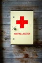 First aid kit with German label emergency kit hangs on wall of raw textured wood planks