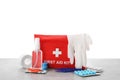 First aid kit, scissors, gloves, pills, plastic forceps and elastic bandage on light grey table against white background