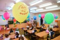 First-form schoolchildren in classroom at school desks on holiday of beginning of elementary school education. Balloons as