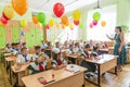 First-form schoolchildren in classroom at school desks on holiday of beginning of elementary school education. Teacher runs first