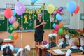 First-form schoolchildren in classroom at school desks on holiday of beginning of elementary school education. Teacher runs first