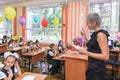 First-form schoolchildren in classroom at school desks on holiday of beginning of elementary school education. Woman teacher runs