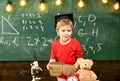 First former interested in studying, education. Kid boy in graduate cap holds book in classroom, chalkboard on