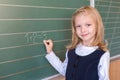 First grade pupil a girl writing on green blackboard at school lesson