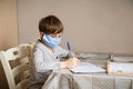 A first-grader boy in a mask is doing homework in quarantine because of a coronavirus Royalty Free Stock Photo