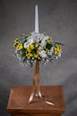 First holy communion flower bouquets. White candle decorated with white,and yellow flowers. Grey backgroud