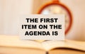 THE FIRST ITEM ON THE AGENDA IS text on paper on the background of an open book with a clock Royalty Free Stock Photo