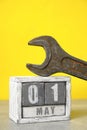 First of May on a calendar made of wood and a wrench in yellow background.Concept Labor Day.