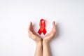 First person top view photo of cupped female hands and red ribbon symbol of aids awareness on white background