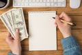 First person top view photo of female hands holding hundred dollars banknotes and pen over notepad cup of coffee keyboard mouse on Royalty Free Stock Photo