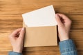 First person top view photo of female hands holding open craft paper envelope with white card on isolated wooden desk background Royalty Free Stock Photo