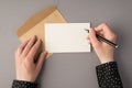 First person top view photo of female hands holding pen over white card open craft paper envelope on  grey background with Royalty Free Stock Photo