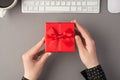 First person top view photo of female hands holding red giftbox with ribbon bow white keyboard mouse and cup of coffee on isolated Royalty Free Stock Photo