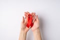 First person top view photo of female hands holding red silk ribbon in crossed palms symbol of aids awareness on white