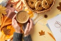 First person top view photo of female hands in jumper holding cup of frothy cocoa over plaid yellow maple leaves anise wicker tray Royalty Free Stock Photo