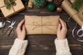 First person top view photo of female hands in sweater holding craft paper package with twine bow giftbox green gold balls pine Royalty Free Stock Photo