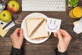 First person top view photo of hand holding sticker note with drawn smiling face over plate with toasts keyboard mouse apples