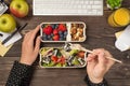 First person top view photo of hand holding tofu on fork over two lunchboxes with salad berries nuts apples glass of juice plant Royalty Free Stock Photo