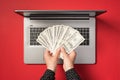 First person top view photo of hands demonstrating fan of one hundred dollar banknotes over open laptop on isolated red background Royalty Free Stock Photo