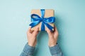 First person top view photo of hands in denim shirt holding craft paper giftbox with vivid blue ribbon bow over sequins on Royalty Free Stock Photo