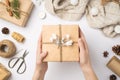 First person top view photo of hands holding craft paper giftbox decorated with twine and snow branch over sweater christmas tree Royalty Free Stock Photo