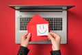 First person top view photo of hands holding red vivid envelope and white sticker note paper with drawn smiling face over open