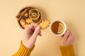 First person top view photo of hands in sweater holding cup of tea with lemon and leaf-shaped cookie over wooden bowl with cookies