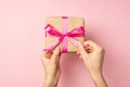 First person top view photo of hands unpacking craft paper giftbox with pink ribbon bow on isolated pastel pink background Royalty Free Stock Photo