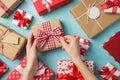 First person top view photo of valentine`s day decor presents and young woman`s hands unwrapping craft paper giftbox with