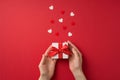 First person top view photo of valentine`s day decorations female hands giving small white giftbox with red dotted ribbon bow and Royalty Free Stock Photo