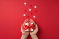 First person top view photo of valentine`s day decorations female hands holding small white giftbox with red dotted ribbon bow on Royalty Free Stock Photo