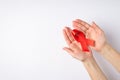 First person top view photo of woman`s hands demonstrating red satin ribbon in palms symbol of aids awareness on white