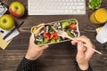 First person top view photo of woman`s hands holding fork and lunchbox with healthy salad over apples glass of juice flowerpot Royalty Free Stock Photo