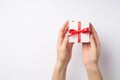 First person top view photo of woman`s hands holding small white giftbox with red dotted ribbon bow on isolated white background Royalty Free Stock Photo