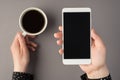 First person top view photo of woman`s hands holding smartphone and cup of coffee on  grey background with copyspace Royalty Free Stock Photo