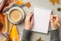 First person top view photo of woman`s hands in jumper writing in notepad cup of coffee on saucer plaid fallen maple leaves pine Royalty Free Stock Photo