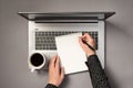 First person top view photo of woman`s hands writing in notepad and cup of coffee on open laptop on isolated grey background with Royalty Free Stock Photo